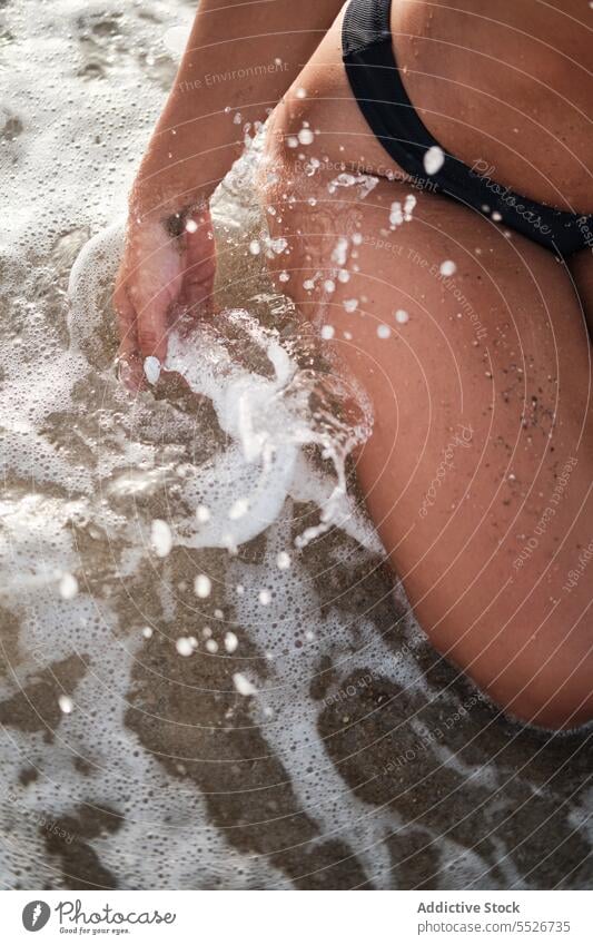 Crop Frau spritzt Meerwasser am Strand am Strand platschen Bikini Bewegung MEER schäumen Urlaub Sommer Wasser winken Küste nass Badebekleidung Ausflug reisen
