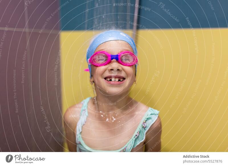 Kind in Badeanzug und Schwimmbrille beim Duschen nach dem Training im Schwimmbad Schwimmer Sport achtsam Schutzbrille Badebekleidung Wellness Vitalität Pool