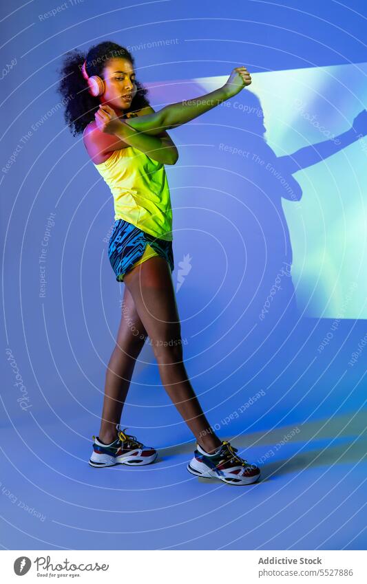 Schwarze Frau mit Kopfhörern im Stehen Studioaufnahme Sport zuhören Musik Fitness Audio Melodie Sportlerin schwarz Afroamerikaner ethnisch meloman Klang