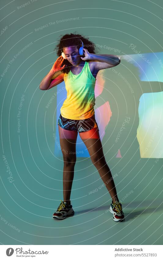 Schwarze Frau mit Kopfhörern im Stehen Studioaufnahme Sport zuhören Musik Fitness ethnisch Audio Melodie Sportlerin meloman Afroamerikaner Klang Sportkleidung