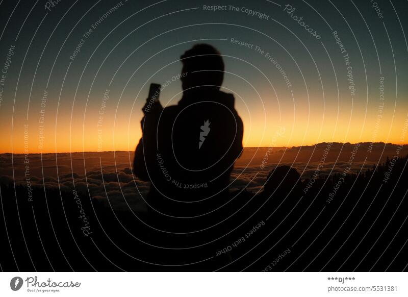 Mann filmt Sonnenuntergang auf einem Berg über den Wolken mit dem Handy Himmel fotografieren filmen Ausblick Aussicht Dämmerung mystisch Licht Abend Kontrast
