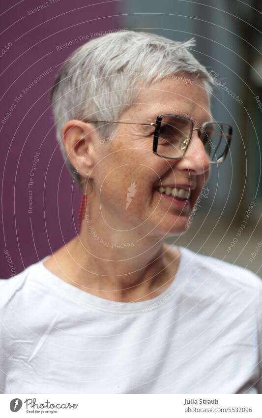 Weites Land | Lachende Frau mit Brille kurze haare grauhaarig Ohrringe Brillenträger lachen freundlich lustig Fröhlichkeit lila weißes T-Shirt Porträt