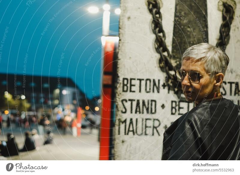 Weites Land | Die Frau blickt vor einem Segment der Mauer kritisch über die Schulter Mauer beleuchtet Berliner Mauer kritischer blick Blick in die Kamera