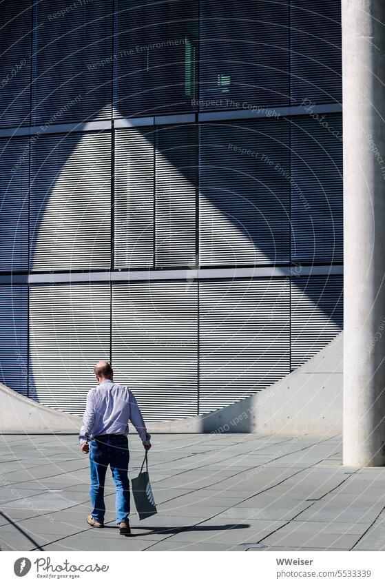 Jemand mit einem Bundestag-Beutel läuft durch das Regierungsviertel von Berlin Ämter Behörden Gebäude Hauptstadt Symbol Bundesadler modern Beton Licht Kontrast