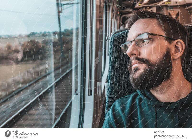 Mann reist allein mit dem Zug und schaut aus dem Fenster männlich Vollbart bärtig Brille Auge reisen Reisender aus dem Fenster schauen Blick nach draußen
