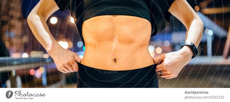 Frau in schwarzer Sportkleidung zeigt muskulösen Bauch abs über Nacht Stadt Hintergrund unkenntlich zeigend Bauchmuskeln Unterleib abdominal Magen passen
