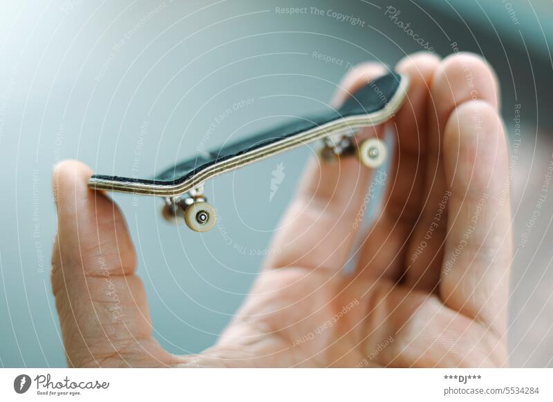 Ein Fingerboard wird in der Hand von Daumen, Zeigefinger und Mittelfinger festgehalten. Sport Miniatur Skateboard Figerboard kleiner Finger Handfläache Nagel