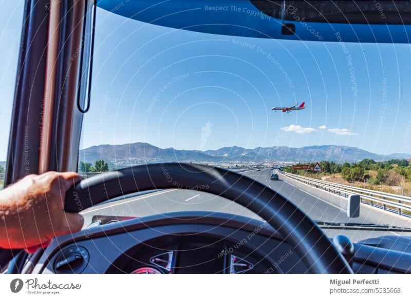 Blick aus dem Führerstand eines Lastwagens auf einer Autobahn, über die ein Passagierflugzeug in geringer Höhe zur Landung ansetzt. im Inneren Lenkrad