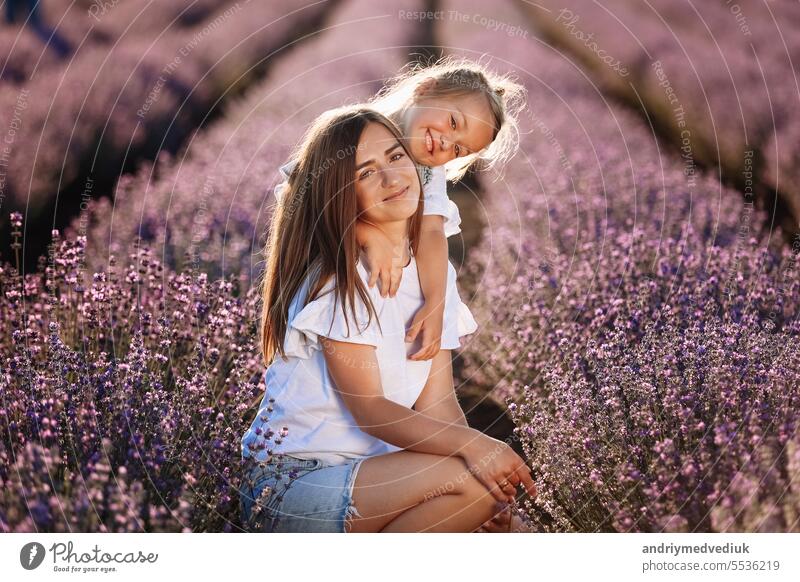 Glückliche Familie in lila Lavendelfeld. junge schöne Mutter und Kind Mädchen genießen zu Fuß blühende Wiese am Sommertag. Mama hat Spaß mit hübschen Tochter in der Natur auf Sonnenuntergang.