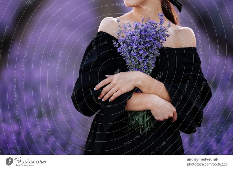 Junge romantische Frau mit gesunder natürlicher Schönheit Haut hält Blumenstrauß in Lavendelfeld. Schönes Mädchen in schwarzem Kleid und Schleife im Haar. Werbung für ein Naturprodukt