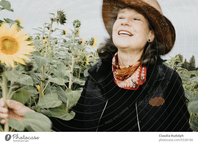 Verschwommene Aufnahme einer lachenden Frau mit Strohhut in einem Sonnenblumenfeld Spätsommer Frühherbst lachende Frau Frau mittleren Alters Gärtnerin Lachen