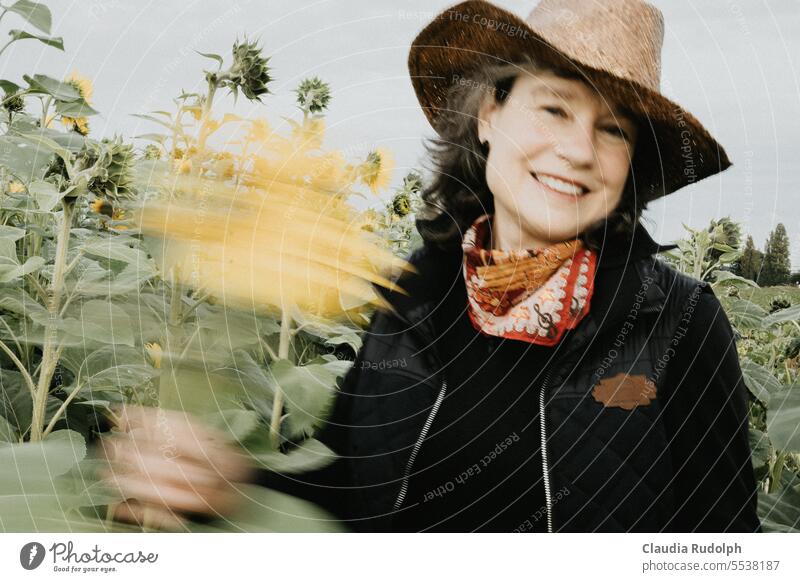 Verwischte Aufnahme einer lächelnden Frau mit Strohhut in einem Sonnenblumenfeld, mit einer Blume winkend Lächeln lächelnde Frau verwischt Sonnenhut Cowboyhut
