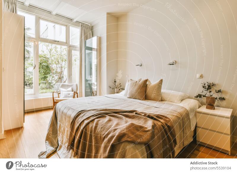 Modernes Schlafzimmer mit Bett und großem Fenster Kopfkissen Decke bequem Ordnung hell modern weiß Wand Textfreiraum Nachttisch Zimmerpflanze Stuhl heimwärts