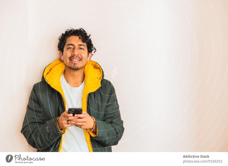 Positiv gekleideter Mann mit Smartphone Ohrstöpsel heiter zuhören Musik formal maskulin Großstadt Porträt Lifestyle Apparatur Gerät Melodie Stil Lächeln