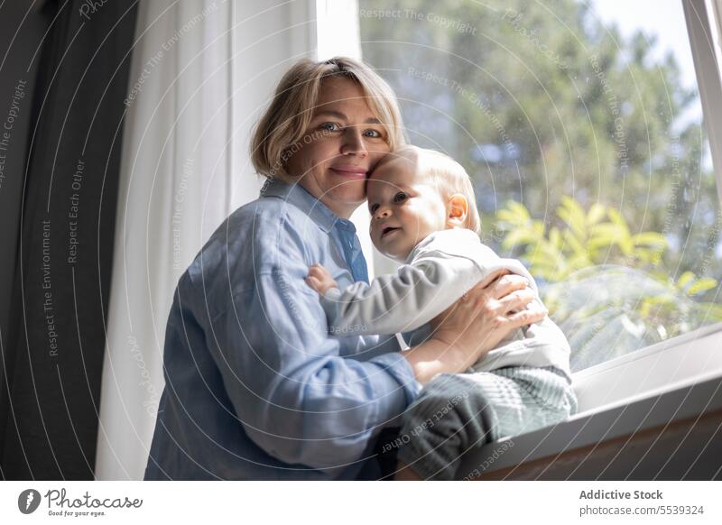 Reife blonde Frau und ein kleiner Junge in der Nähe des Fensters zu Hause Mutter Baby Säugling Kind Liebe Pflege Kinderbetreuung Eltern Mutterschaft Kindheit