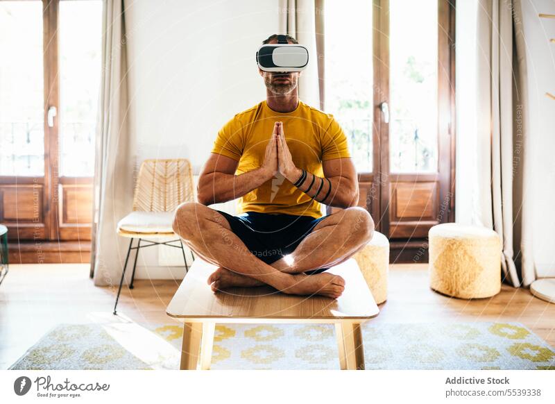 Mann mit VR-Headset trainiert in hellem Raum Yoga Lotus-Pose Virtuelle Realität üben meditieren Schutzbrille männlich digitale Entgiftung Cyberspace Achtsamkeit