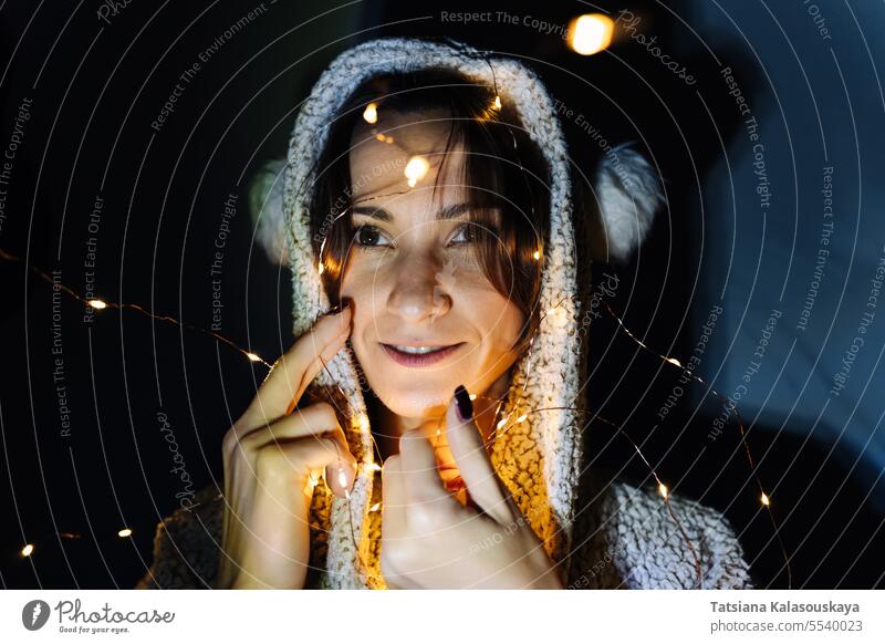 Porträt einer jungen Frau in einem mit einer Lichterkette geschmückten Zimmer mit Kapuze Raum dekoriert Schnur beleuchtet verwickelt Nacht dunkel Kopf Abend