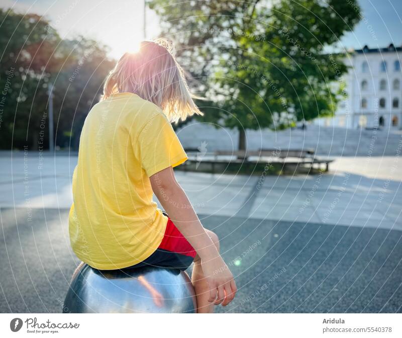Kind dreht sich sitzend auf einer Metallkugel in der Stadt bei Gegenlicht Junge Blond Haare & Frisuren Park Kopf Außenaufnahme Jugendliche Hinterkopf Platz