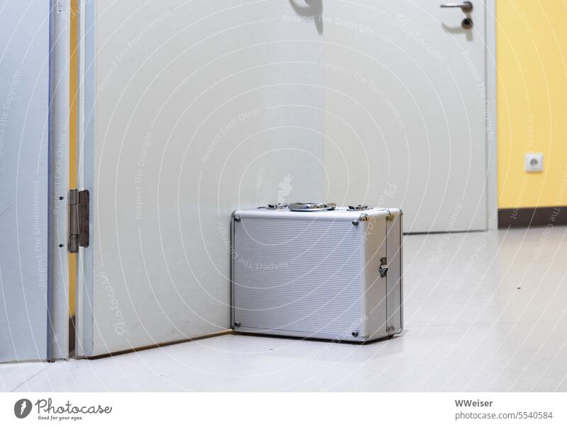 Ein geschlossener Werkzeugkoffer steht auf dem Boden des Flurs und hält die Tür zum Zimmer auf Koffer Techniker Zubehör Instrumente geschützt Korridor Raum