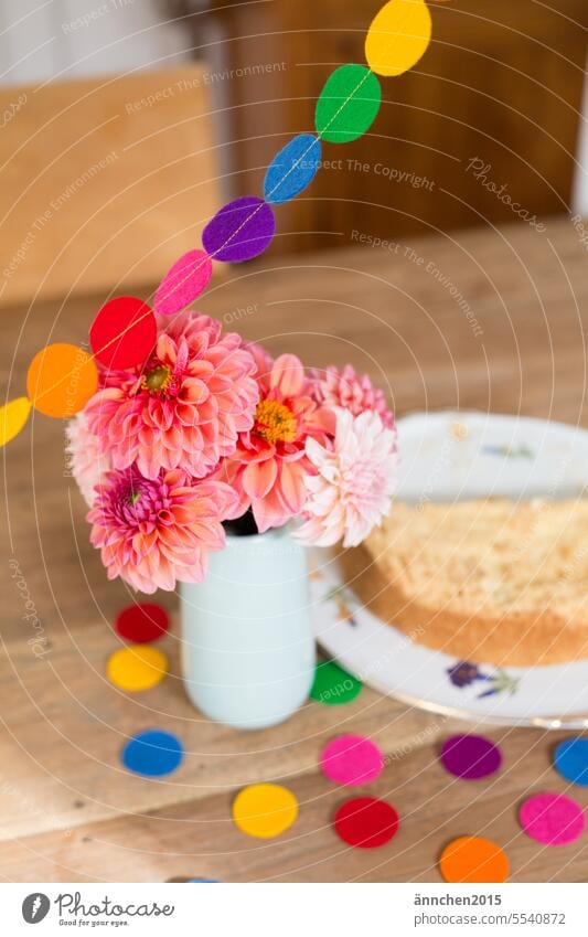ein Strauß mit Dahlien steht auf einem Holztisch daneben steht ein Kuchen und man sieht eine bunte Girlande und buntes Konfetti Geburtstag feiern fröhlich
