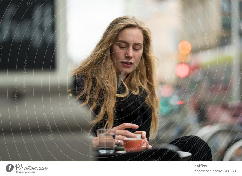 eine junge Frau in einem Straßenkaffee blickt nachdenklich freundlich auf die Kaffeetasse in ihrer Hand Frauengesicht Junge Frau Erwachsene Porträt Jugendliche