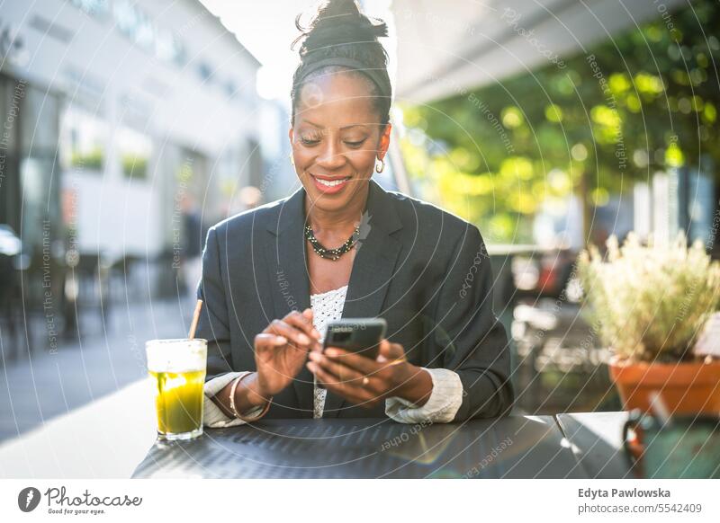Porträt einer lächelnden Geschäftsfrau, die in einem Café im Freien ein Mobiltelefon benutzt Menschen Stadtzentrum Business Freude Frau urban schwarz natürlich