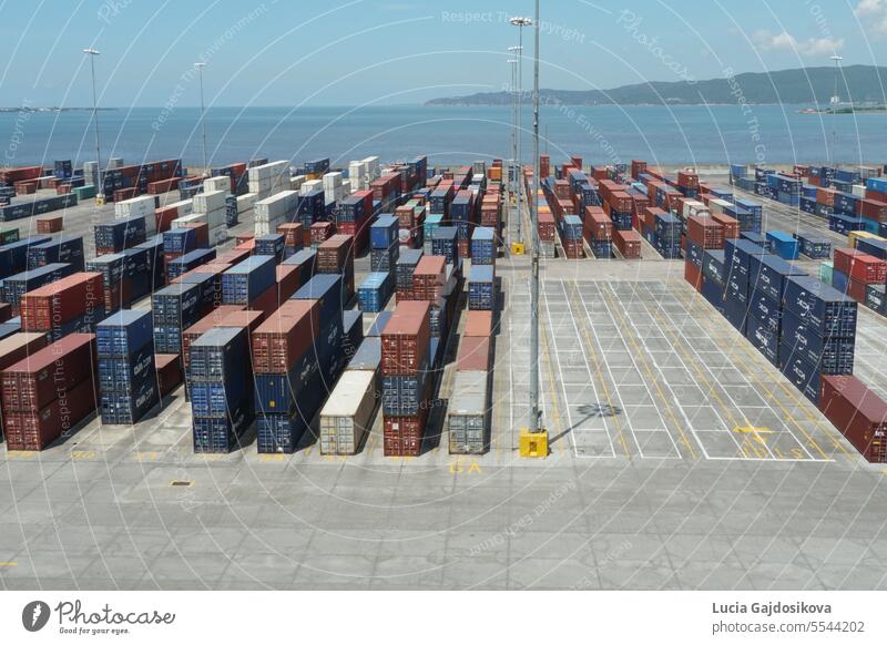 Im Hafen von Kingston, dem berühmtesten Seehafen Jamaikas, reihen sich Containerterminals mit Kisten von verschiedenen Verladern aneinander. Dahinter liegen Hügel und der Atlantik.