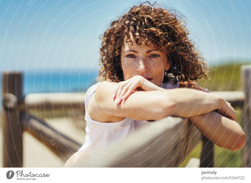 Junge Frau lehnt an einem hölzernen Geländer am Meer Windstille sich[Akk] entspannen besinnlich fettarm Zaun ruhig krause Haare Urlaub friedlich Küste Kälte