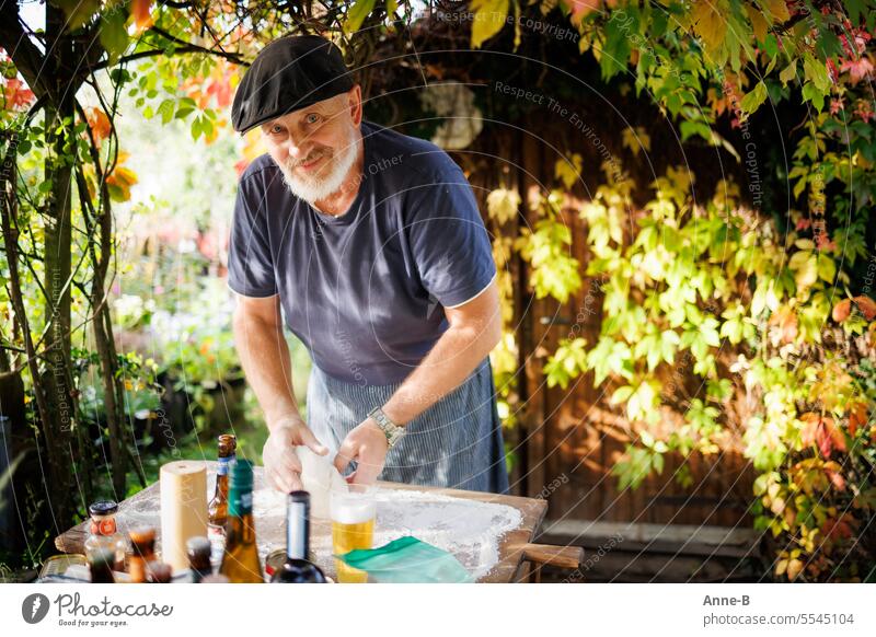 Die Pizzasaison im Garten geht langsam zu Ende. Freundlicher Mann mit Bart beim Teig kneten , um ihn herum wilder Wein in beginnender Herbstfärbung. selfmade