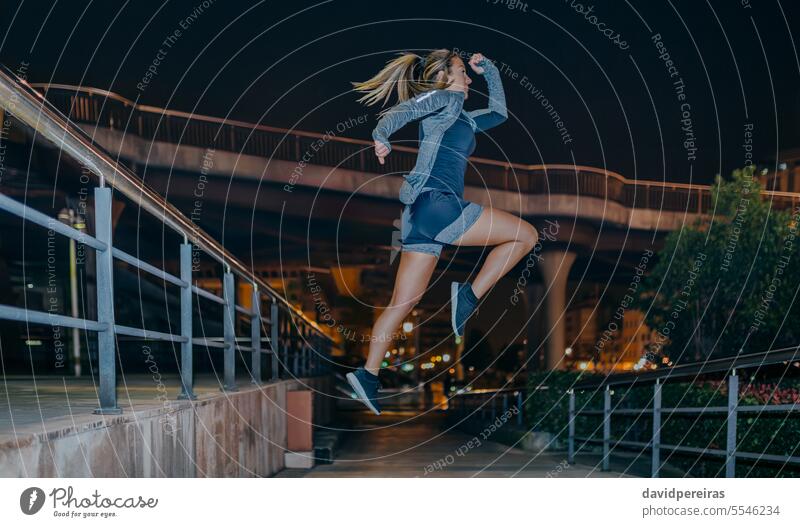 Frau springt beim Kardio-Training in der Stadt bei Nacht springend Übung Herz Sport Tun jung fliegen leer urban Großstadt Textfreiraum Kopie Raum rechts Aktion