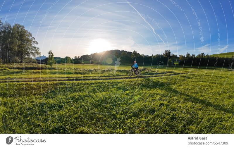 Weitwinkelaufnahme von einer Frau die im Gegenlicht der Sonne radfährt bombig Sport radfahren Fahrrad sich[Akk] beugen gegenlicht Sonnenlicht fahrradfahrerin