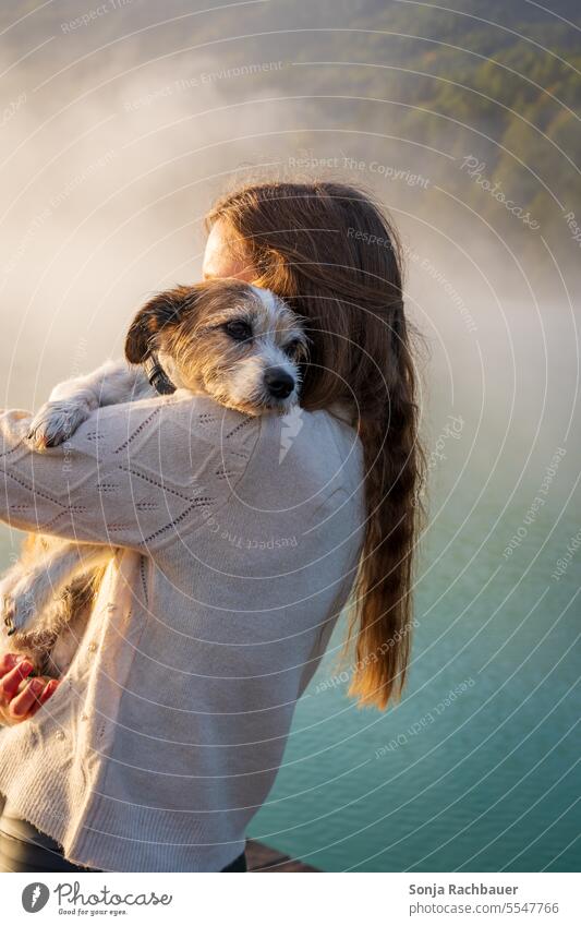 Ein kleiner Hund liegt auf der Schulter einer jungen Frau an einem See Haustier Freundschaft Liebe Zusammensein Tier Glück Lifestyle niedlich Umarmen