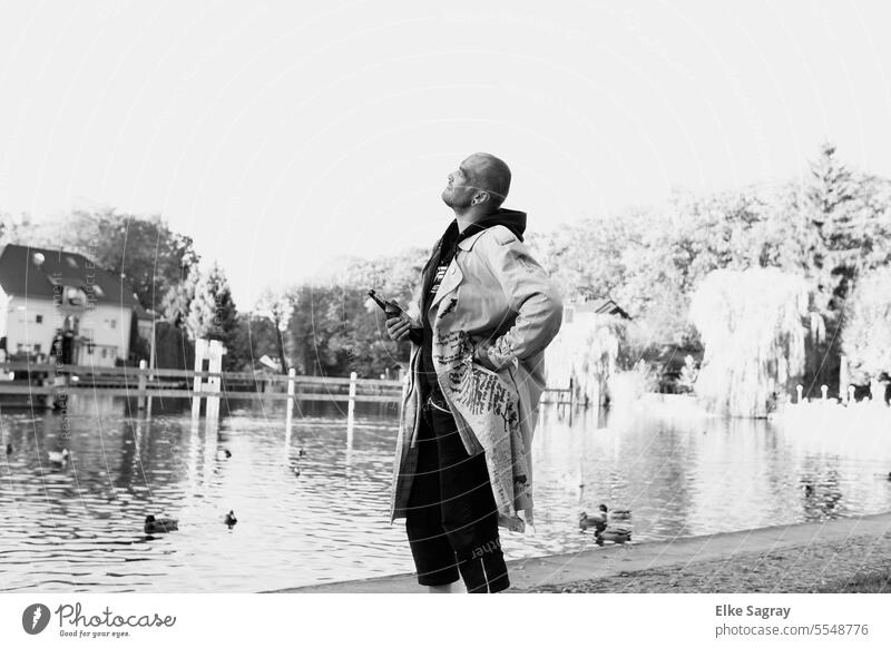 Mann am Wasser blickt in den Himmel schwarz weiß Foto Junger Mann Jugendliche Außenaufnahme langer Mantel wasser 18-30 Jahre Lifestyle maskulin schön Porträt