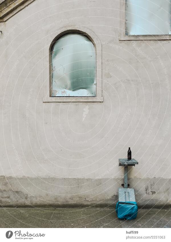 Urbanes Stillleben mit Mülleimer, Bierflasche und Fenstern vor einer grauen, tristen Wand urbanes Stillleben Flasche Pfandflasche Glas abstrakt aufgeräumt