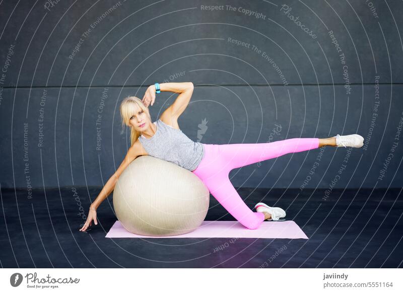 Erwachsene Frau macht Übungen auf dem Boden eines Fitnessstudios mit einem Fit-Ball Training Bein angehoben Unterlage Stock Lügen Erwachsener Wellness üben