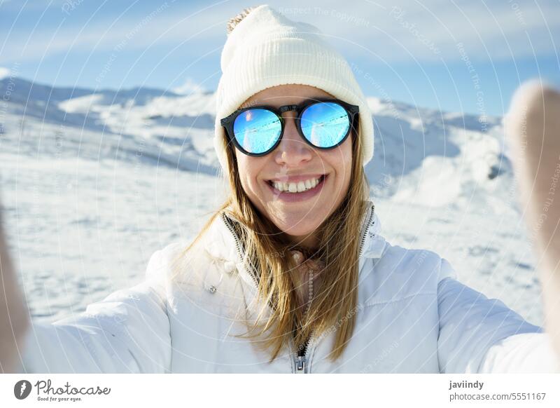 Fröhliche Frau mit Sonnenbrille macht Selfie in verschneiten Bergen Winter Berge u. Gebirge Lächeln Schnee Glück warme Kleidung Berghang fotografieren jung