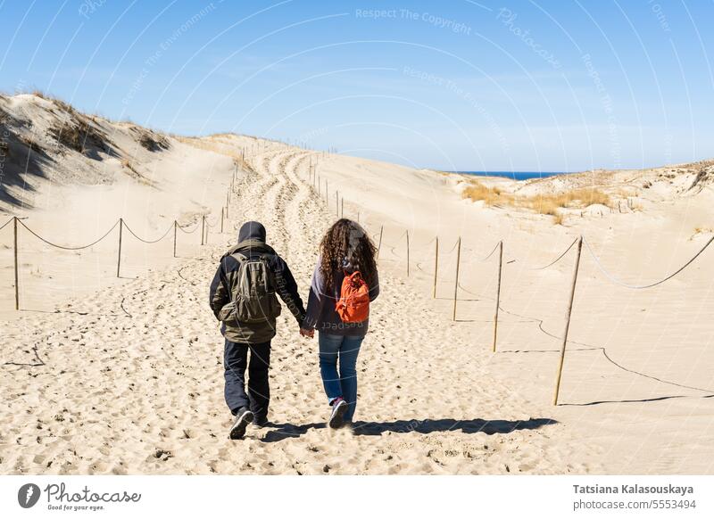 Ein Mann und eine Frau gehen Hand in Hand über die Sanddünen auf der Kurischen Nehrung nahe der Ostsee Paar Backpacker Touristen reisen Dunes Ufer männlich