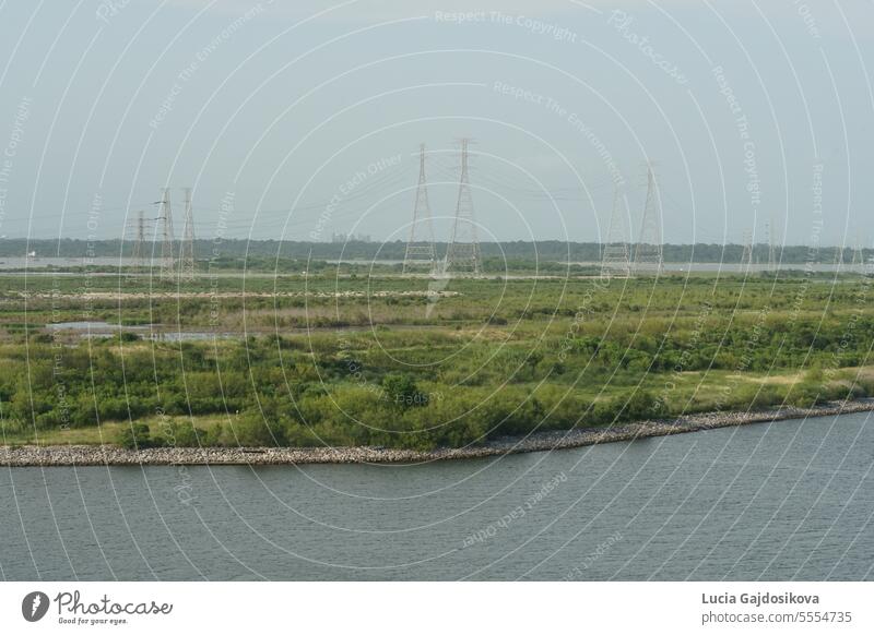Hohe Strommasten auf einer grünen Wiese vom Containerterminal des Hafens von Houston aus gesehen. Hintergrund blau Kabel Küste elektrisch Elektrizität Energie