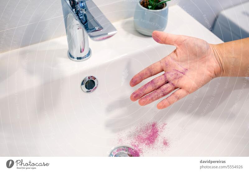 Nahaufnahme einer nicht erkennbaren Frau, die lila Glitzer von ihrer Hand in ein Waschbecken im Badezimmer entfernt unkenntlich Entfernen Reinigen Glitter Mikro
