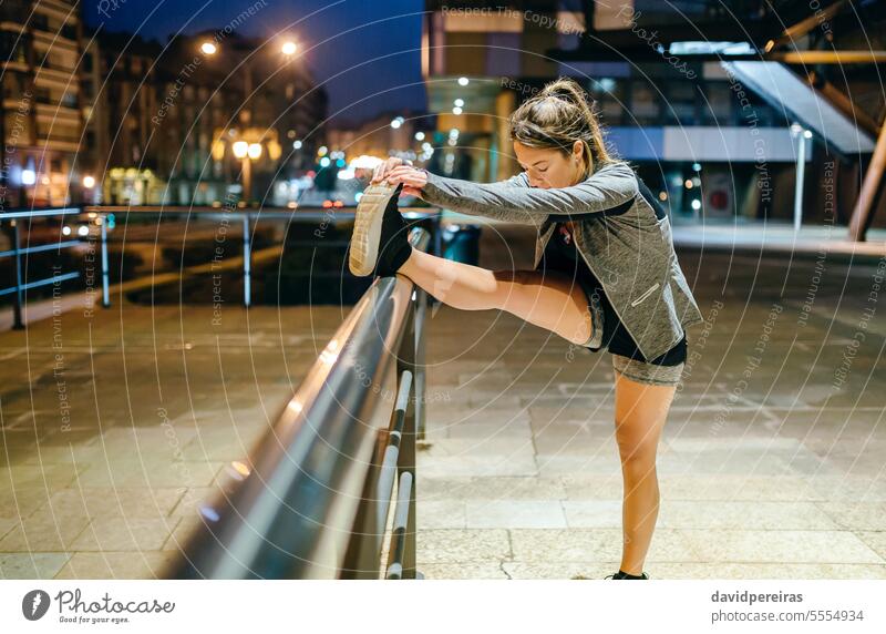 Läuferin dehnt ihr Bein vor dem Training bei Nacht in der Stadt Frau strecken Erwärmung nach oben Übung Abend Treppengeländer Reling blond jung Pferdeschwanz