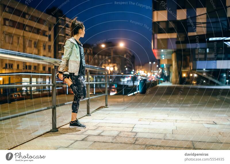 Läuferin, die sich vor dem nächtlichen Training in der Stadt die Beine am Geländer vertritt unkenntlich Frau strecken Übung Nacht Großstadt leer jung brünett