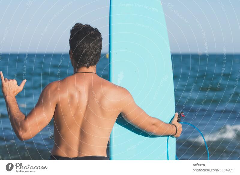 Ein Mann steht am Ufer und hält ein Surfbrett - Ansicht von hinten männlich Person Sport Surfer Lifestyle Strand MEER Brandung Surfen Sand Meer Holzplatte