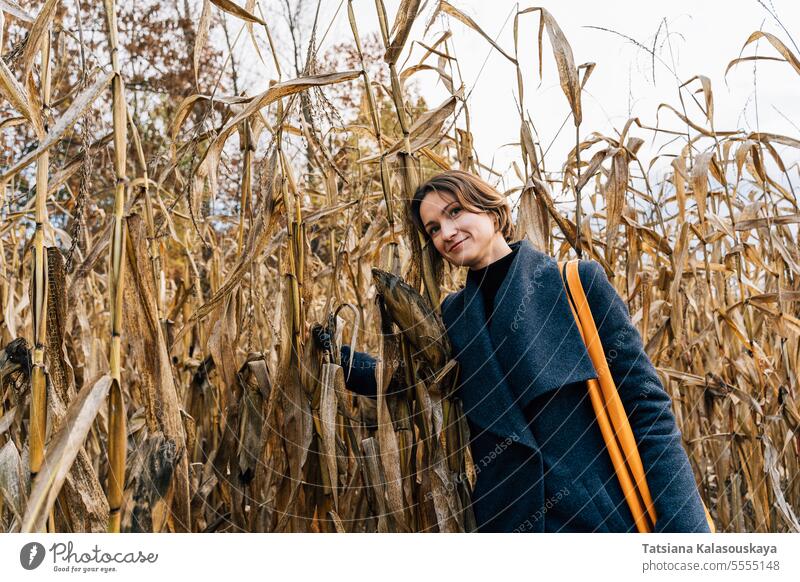 Frau umarmt trockene Maisstängel in einem Maisfeld im Herbst umarmend trocknen Stängel Kornfeld Mantel Reihen Feld fallen im Freien ländlich Landschaft Ernte