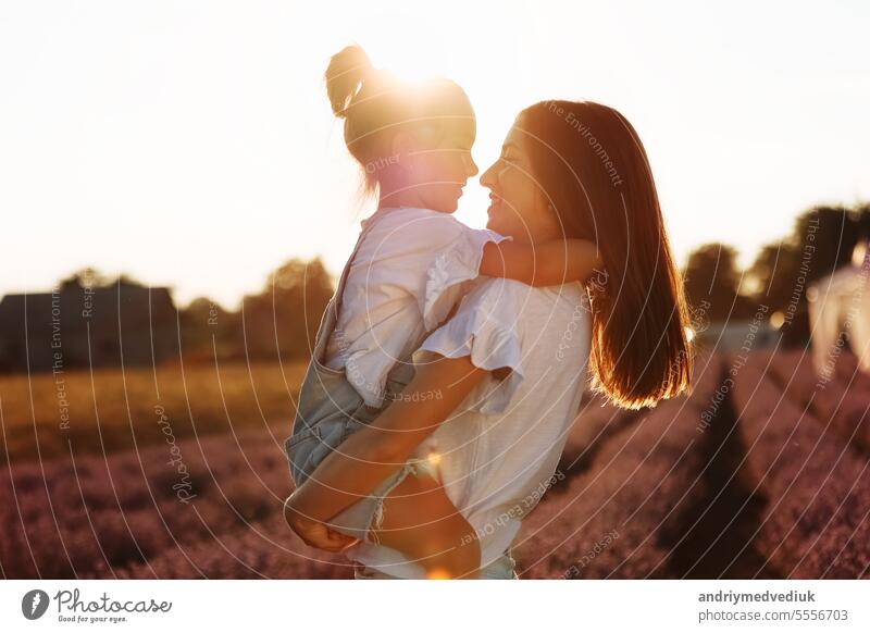 Familie Tag. junge Mutter und kleine Tochter genießen Sie in einem Feld mit Lavendel bei Sonnenuntergang entspannen. Eine schöne Mutter umarmt und küssen Kind Mädchen fest. Mütterliche Pflege und Liebe für das Kind. Muttertag