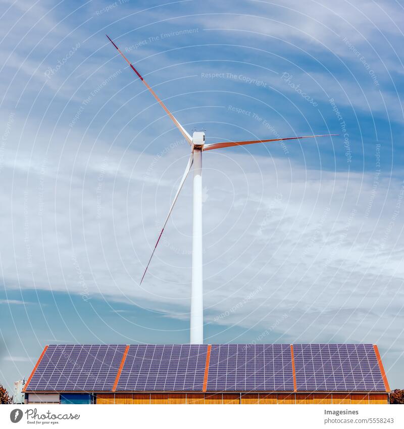 Sonnenkollektoren auf einem Dach einer Industriehalle und eine Windkraftanlage auf einem Feld alternative Energie blau Gebäude Solarzellen Kopierraum