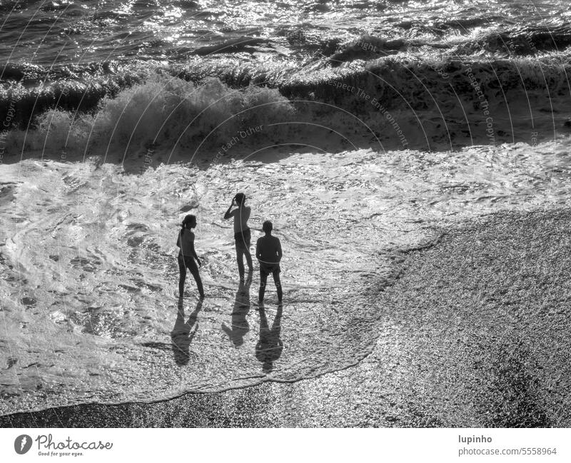 Drei Kinder stehen in der Meeresbrandung drei Gischt Gegenlicht schwarzweiß vonoben Schaum Welle Herbst Urlaub Küste Ligurien Schatten