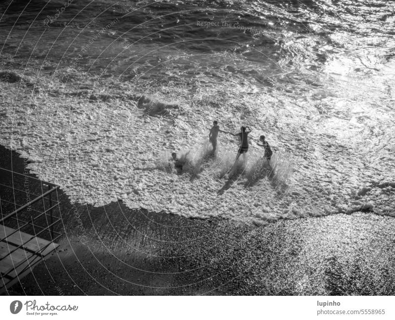Drei Kinder spielen in der Meeresbrandung drei Schaum Gischt Welle schwarzweiß silbern gegenlicht vonoben Urlaub spaß Sand Kiesel