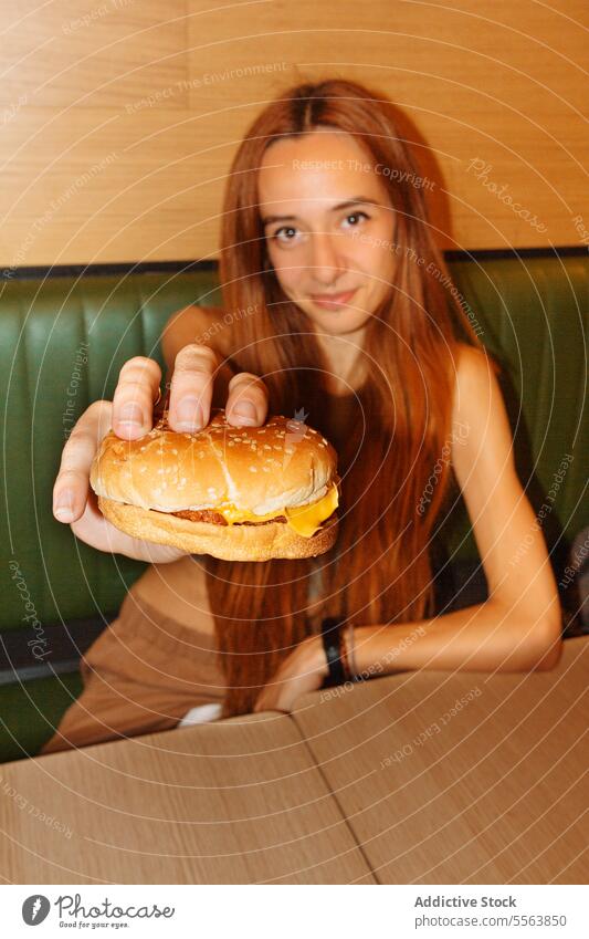 Junge Frau zeigt Hamburger Mädchen essen Fastfood Burger jung Lebensmittel Tisch Sitzen eine Abendessen Mittagessen Snack Beteiligung Hand ungesund Ernährung