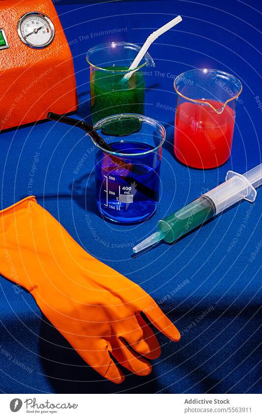 Chemische Getränke auf blauem Tisch neben Maschinenhandschuh und Spritze trinken bearbeitet Chemikalie Labor Cocktail chemisch Glas Stillleben kreativ