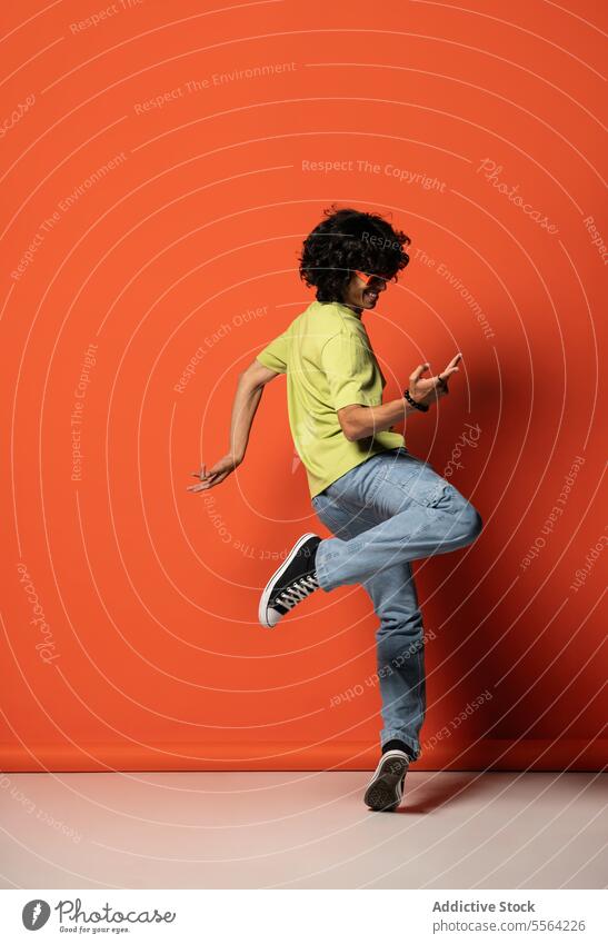 Junger Mann mit dunklem Haar tanzt in der Nähe der roten Wand Tanzen Bein angehoben Tänzer Schatten ausführen sich[Akk] bewegen beweglich Licht Energie männlich